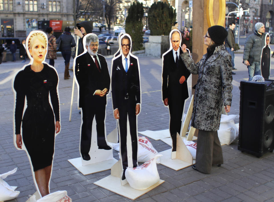 A woman gestures to cardboard image of Russian President Vladimir Putin surrounded by cardboard images of candidates for the Ukraine presidential election, in central Kiev, Ukraine, Thursday, March 28, 2019. Ukraine will hold presidential elections on March 31. (AP Photo/Sergei Grits)