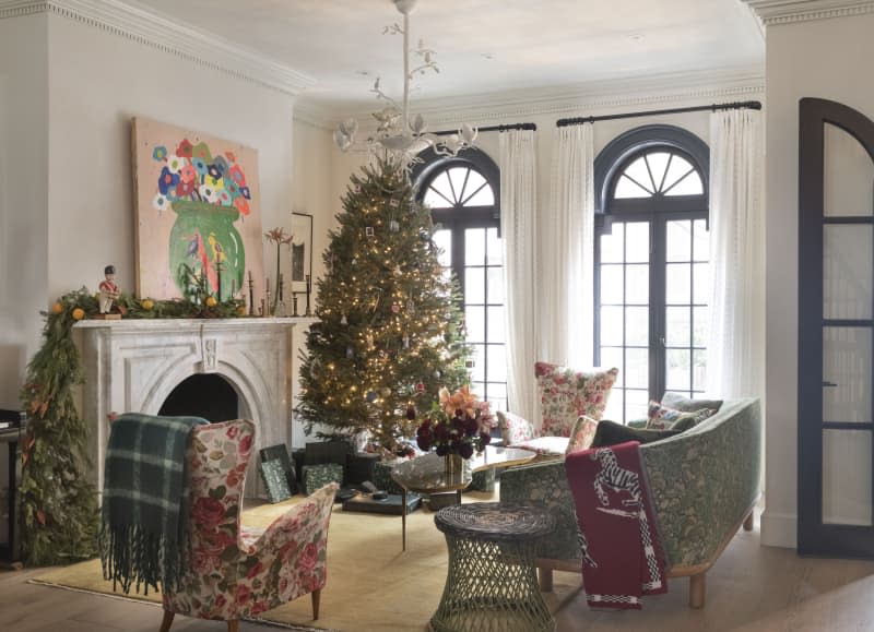 A living room with a large Christmas tree across from two floral chairs and a floral curved couch