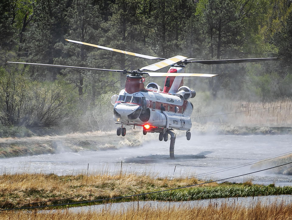 A chinook helicopter draws water from a pond along Highway 434 to drop on a nearby ridge as firefighters from all over the country converge on Northern New Mexico to battle the Hermit's Peak and Calf Canyon fires on May 13, 2022. (Jim Weber/Santa Fe New Mexican via AP)