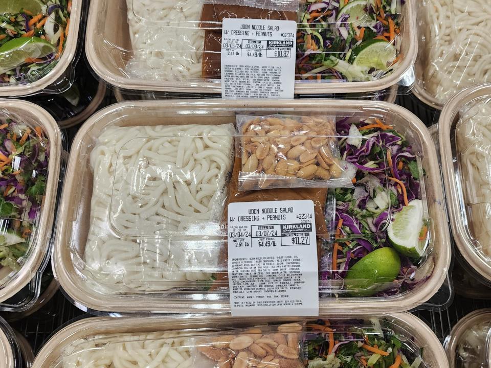 Clear containers of Udon noodles with a salad containing carrots and purple cabbage, peanut sauce, and peanuts at Costco