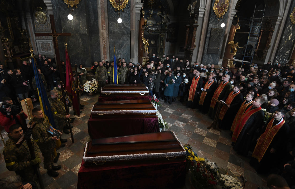 A row of coffins surrounded by clergy, mourners and soldiers at a church. 