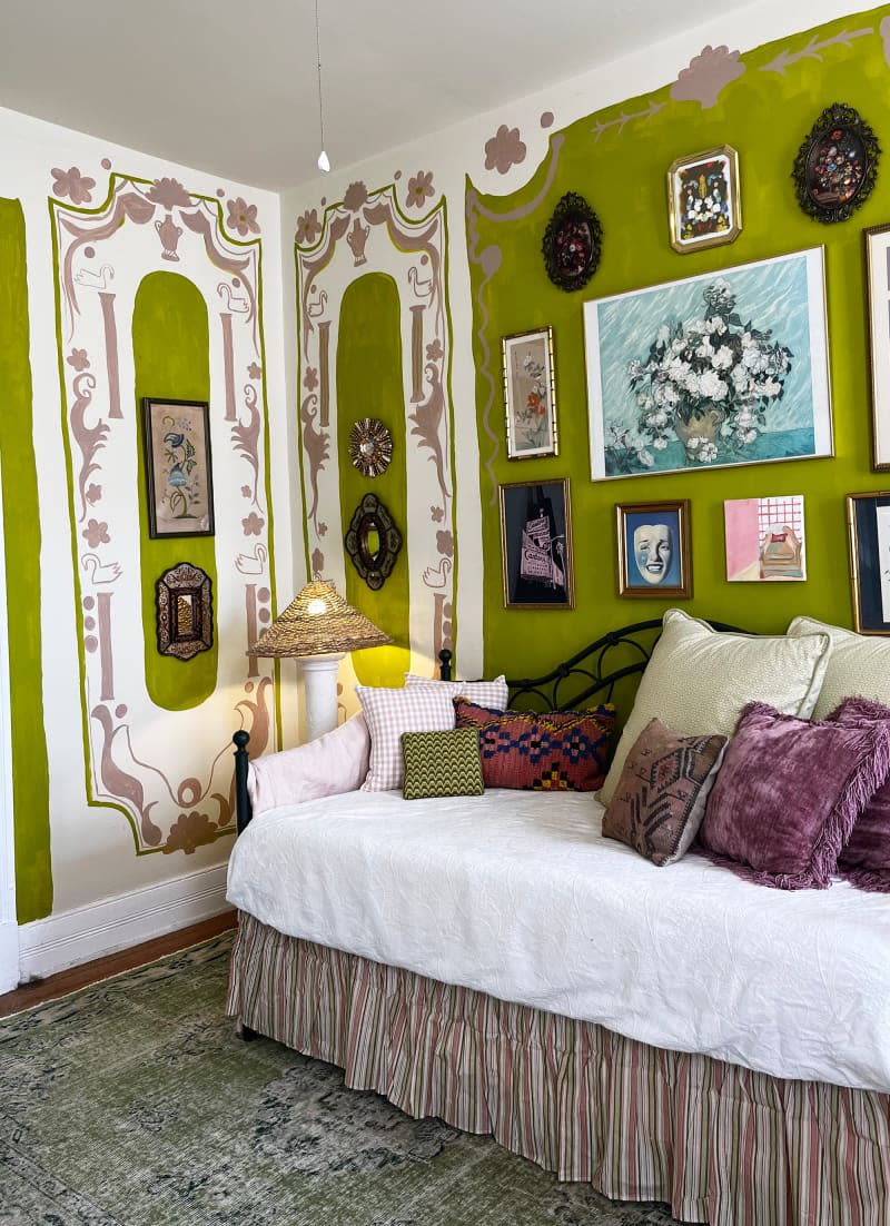 View of skirted daybed in front of green wall with decorative paint and hung artwork.
