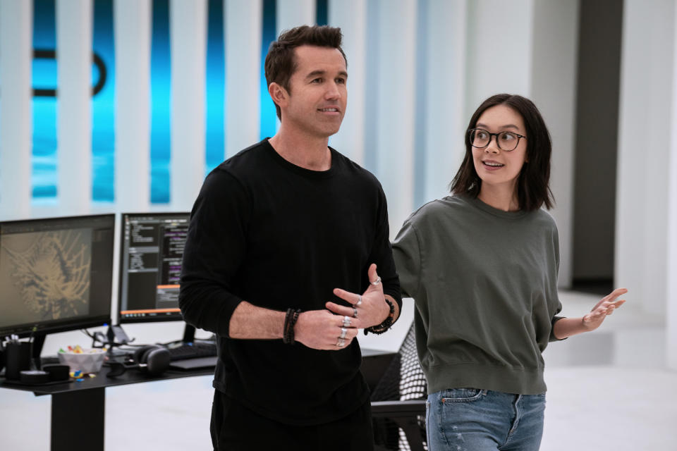 a man and a woman standing in front of a computer and the woman gesturing toward him