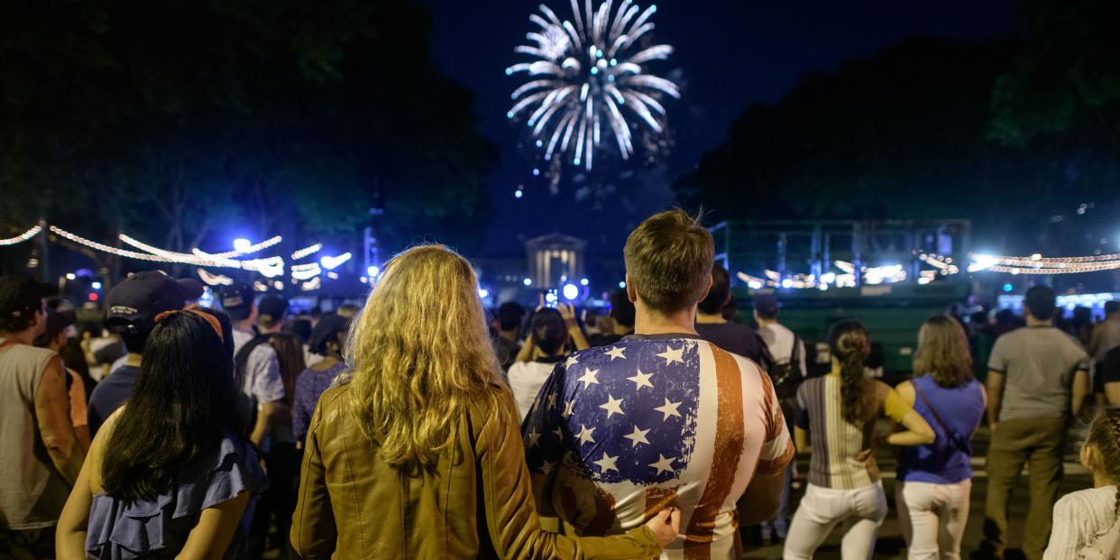 couple, one wearing an american flag shirt, watching fireworks in a crowd