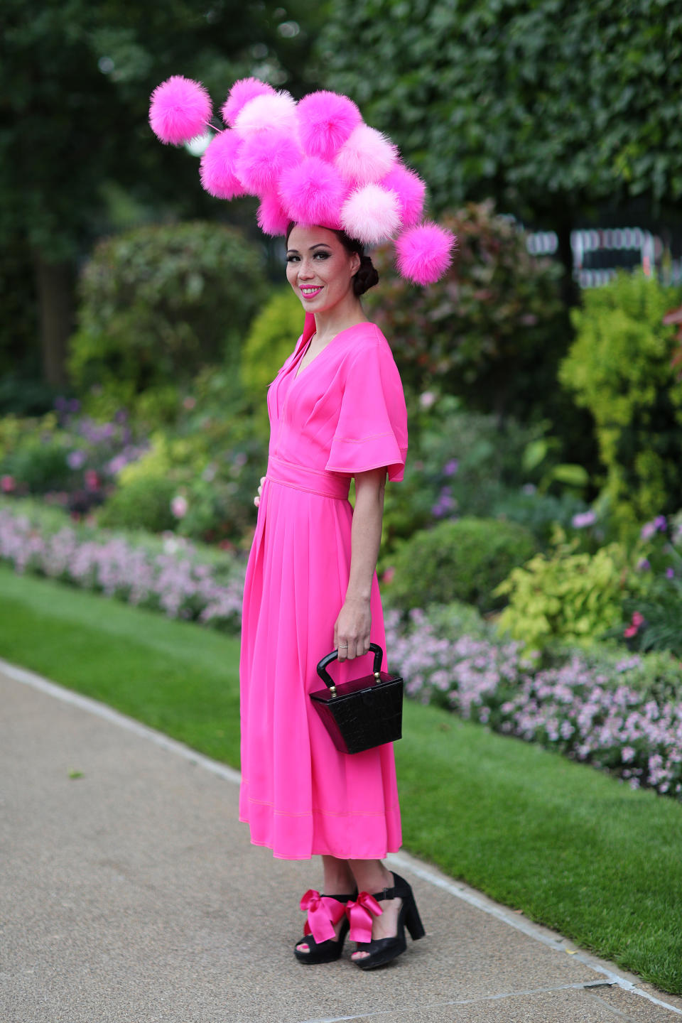 Racegoer Heather Morris pairs a giant fluffy, pom pom hat with a hot pink dress at a Staud bag (<a href="https://fave.co/2XX8hrg" rel="noopener" target="_blank" data-ylk="slk:currently on sale for £189;elm:context_link;itc:0;sec:content-canvas" class="link ">currently on sale for £189</a>). <em>[Photo: Getty]</em>