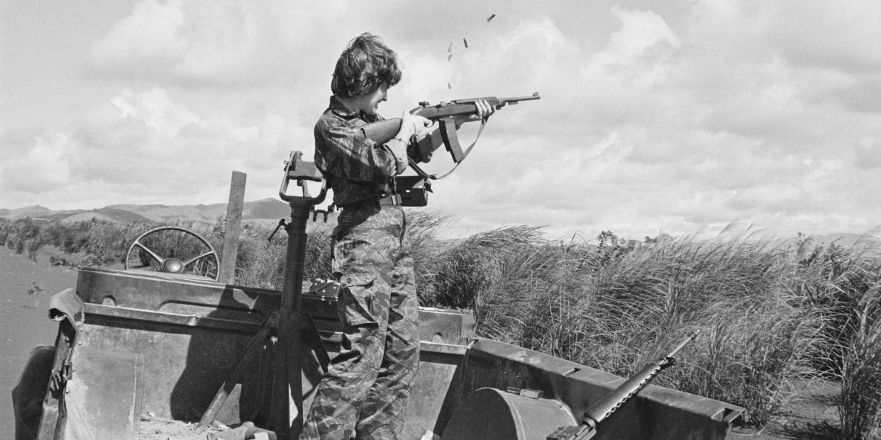 Reporter Betsy Halstead stands on the bed of a truck holding an M16 automatic rifle