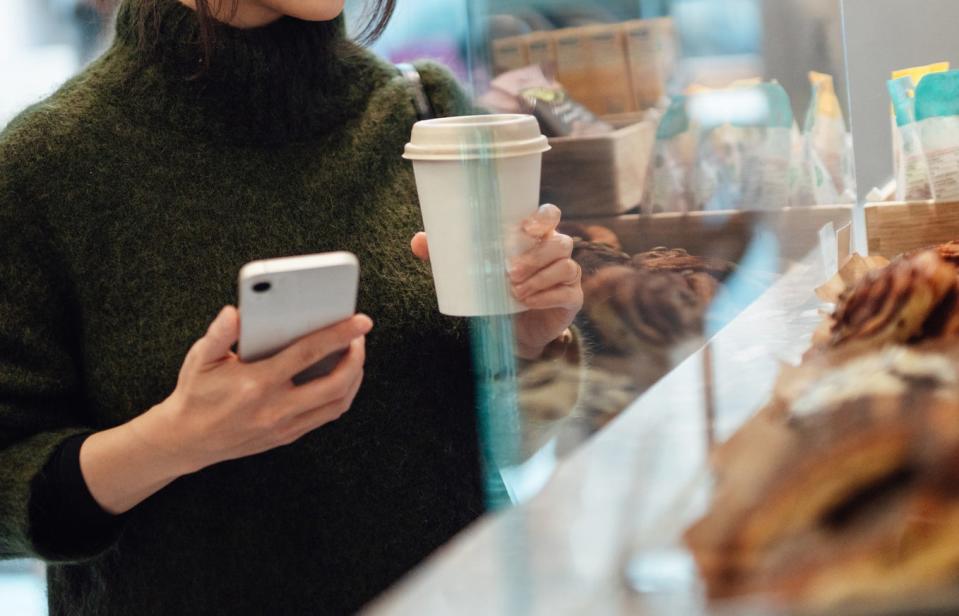 person holding a coffee in front of a bakery display