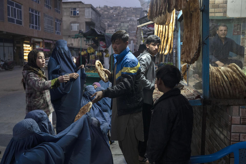 FILE - A man distributes bread to Burka-wearing Afghan women outside a bakery in Kabul, Afghanistan, Thursday, Dec, 2, 2021. Pakistan is rallying Muslim countries to help Afghanistan stave off an economic and humanitarian disaster while also cajoling the neighboring country's new Taliban rulers into concessions to soften their image abroad. (AP Photo/Petros Giannakouris, File)