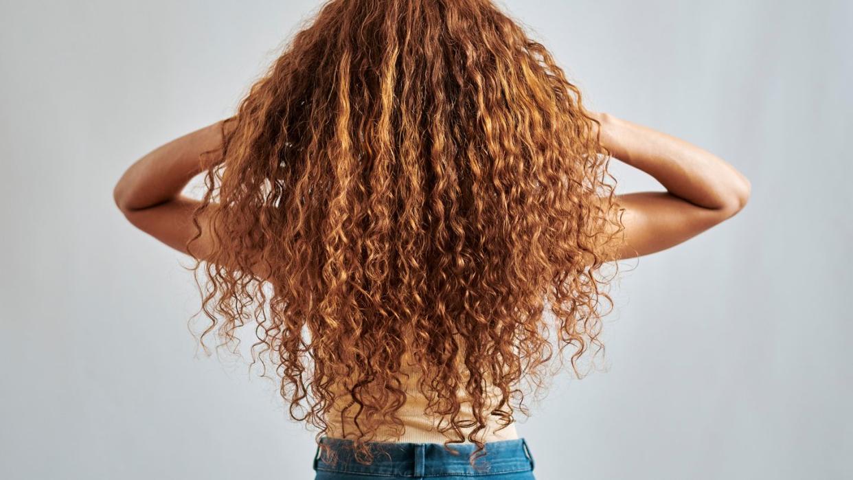 woman with healthy, natural and ginger hair with relax curly, auburn or red beauty hairstyle back view shampoo salon hair care or redhead girl playing with clean red hair isolated on grey background