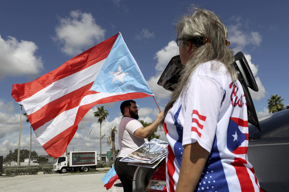 Aaron and Diana Umpirerre gather in the parking lot to meet others to head to West Palm Beach for a protest, Saturday, Sept. 22, 2018 in Hollywood, Fla. Activists marking the one-year anniversary of Hurricane Maria's devastation of Puerto Rico are staging a rally and caravan focused on President Donald Trump's Mar-a-Lago resort in Florida. (Mike Stocker /South Florida Sun-Sentinel via AP)