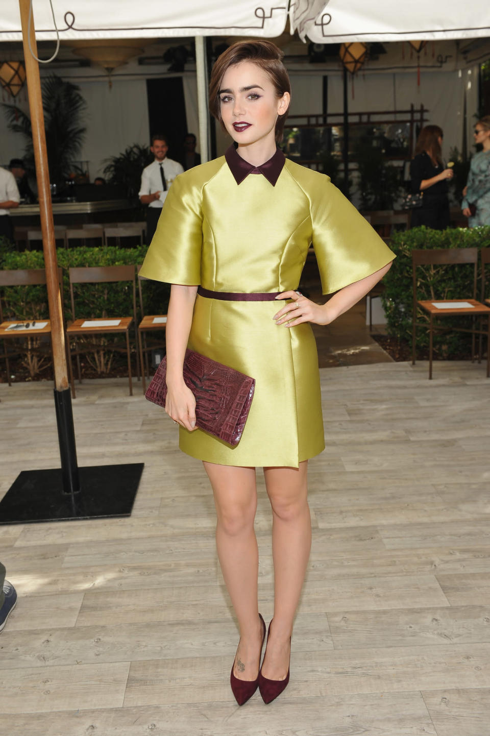 Lily Collins wears a chartreuse satin dress with oxblood accents at the CFDA/Vogue Fashion Fund Show.