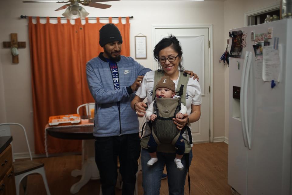 A man supports a woman as she walks with her baby carrier.