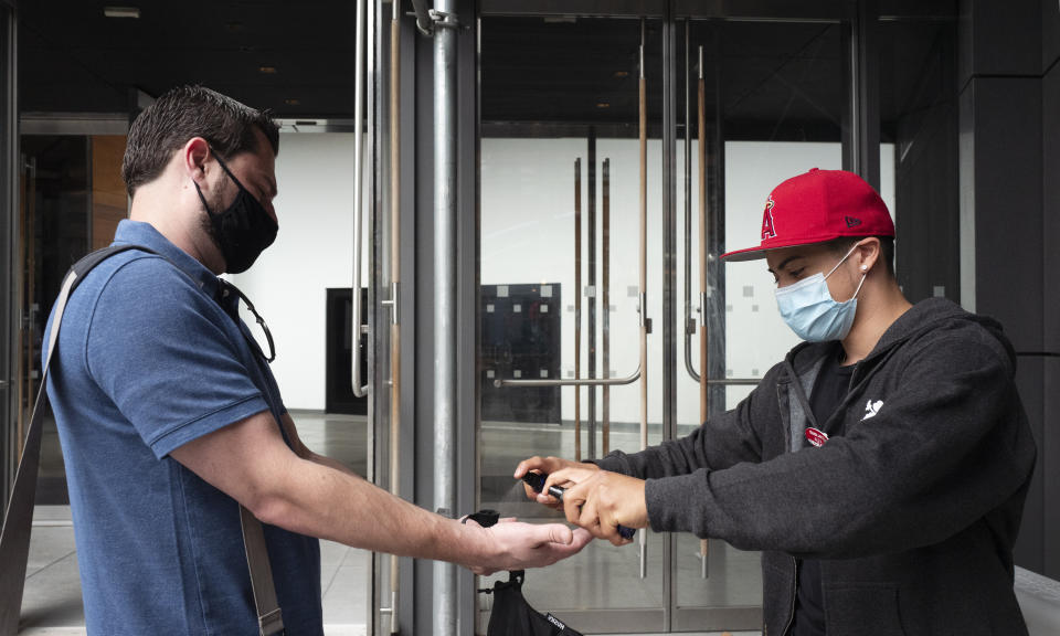 A Trader Joe's store employee, right, sprays hand sanitizer on a customer before he enters the Brooklyn supermarket, Tuesday, June 30, 2020, in New York. New York City may begin Phase 3 reopening as early as Monday, July 6. (AP Photo/Mark Lennihan)