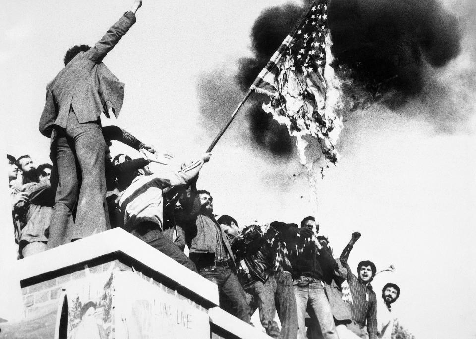 Image: Demonstrators perched atop of the United States Embassy wall burn an American flag, the fourth American flag to be burned since the students seized the embassy and more than 60 hostages (Bettmann Archive / Getty file)