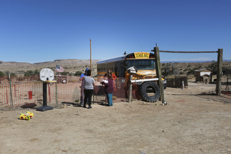 Social worker Victoria Dominguez, background right, delivers supplies she collected at Cuba High School, to deliver along a rural school bus route outside Cuba, N.M., Oct. 19, 2020. The switch to remote learning in rural New Mexico has left some students profoundly isolated — cut off from others and the grid by sheer distance. The school system is sending school buses to students’ far-flung homes to bring them assignments, meals and a little human contact. (AP Photo/Cedar Attanasio)