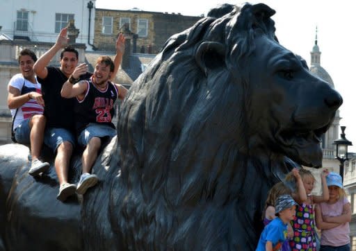 Tourists sit on a lion statue as they pose for photos at Trafalgar Square in central London. Prime Minister David Cameron insisted Thursday that Britain would deliver a memorable Olympics after US presidential hopeful Mitt Romney backtracked on barbed comments he made about the London Games