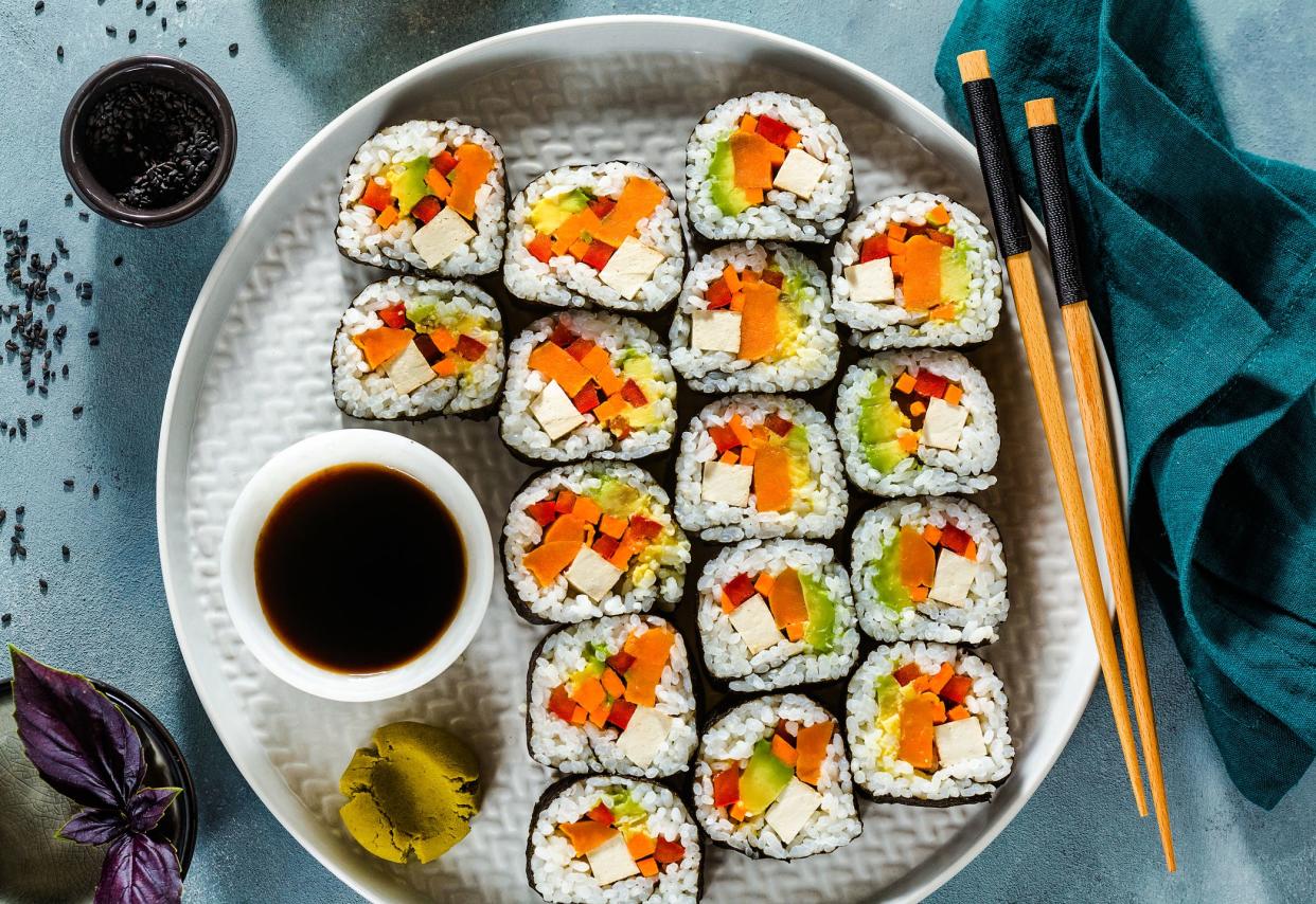 Vegetarian sushi on a white porcelain plate with chopsticks, soy sauce, and wasabi on a blue table with matching tablecloth