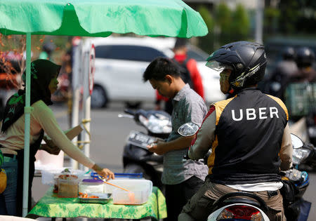 An Uber motorcycle taxi driver stops at a food stall next to a shopping mall in Jakarta, Indonesia September 20, 2017. REUTERS/Darren Whiteside