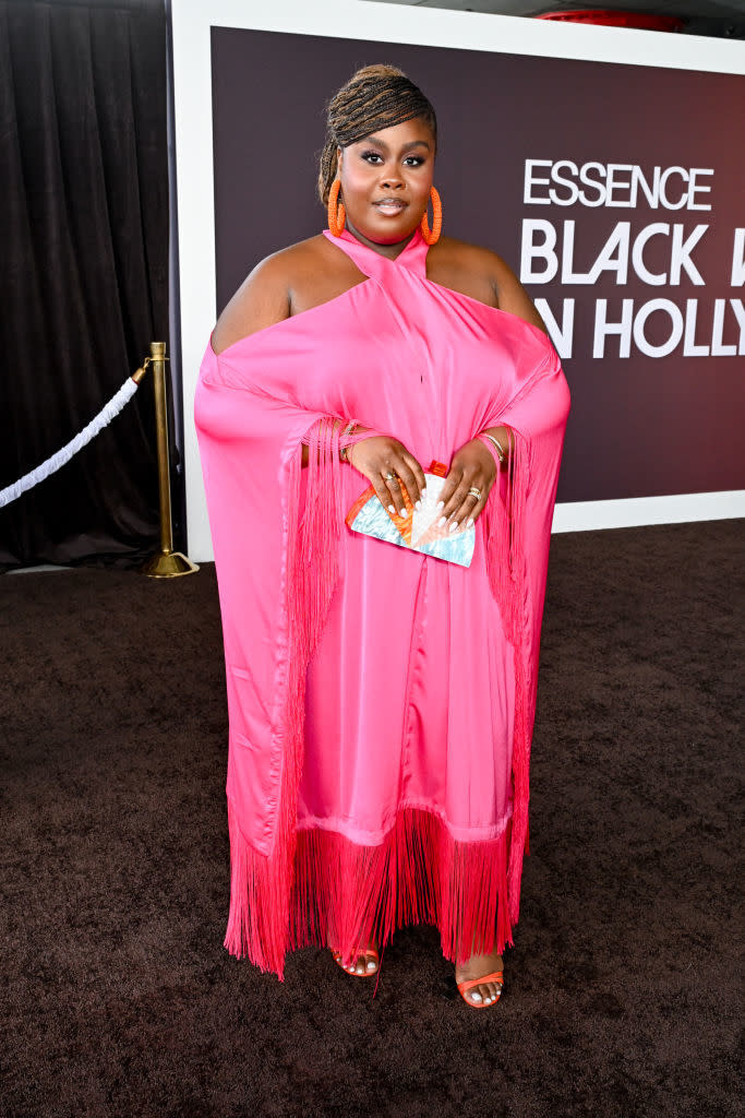 Raven in a fringed gown and sandals poses with a clutch on the red carpet