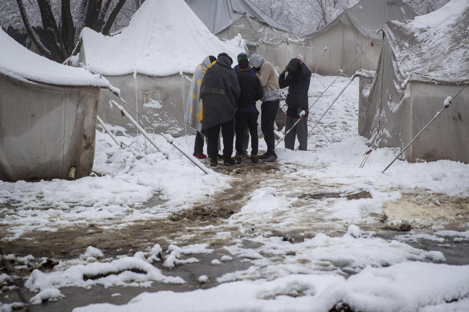 A group of migrants stand amid snow covered tents at the Vucjak refugee camp outside Bihac, northwestern Bosnia, Tuesday, Dec. 3, 2019. A top European human rights official has demanded immediate closure of a migrant camp in Bosnia where hundreds of people have refused food and water to protest lack of protection in snowy and cold weather. (AP Photo/Darko Bandic)