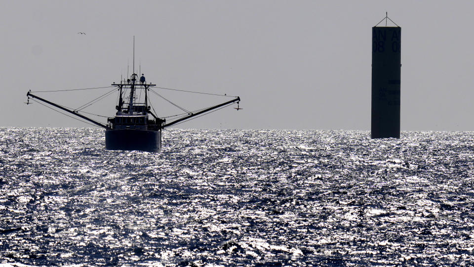 The fishing vessel New Horizon motors, with outriggers out for balance, past a monopile structure for an offshore wind farm project, while working with foreign ships, Tuesday, July 11, 2023, off the coast of Rhode Island. The trade association that represents the offshore service industry is going to great lengths to make sure that jobs go to Americans as the U.S. offshore wind industry ramps up. (AP Photo/Charles Krupa)