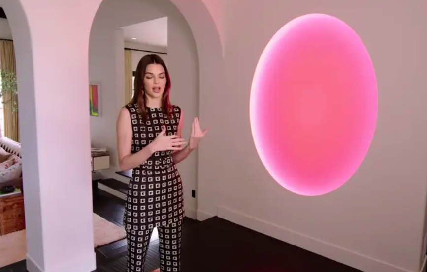 Kendall standing next to the art piece which is a large circle in her wall that emits a neon light