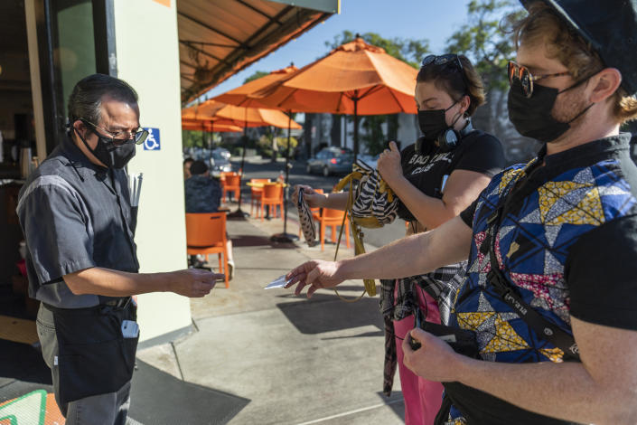 Waiter Juan Rodrigues, left, asks patrons to show their vaccination cards before entering the Fred 62 restaurant in the Los Feliz neighborhood of Los Angeles. 