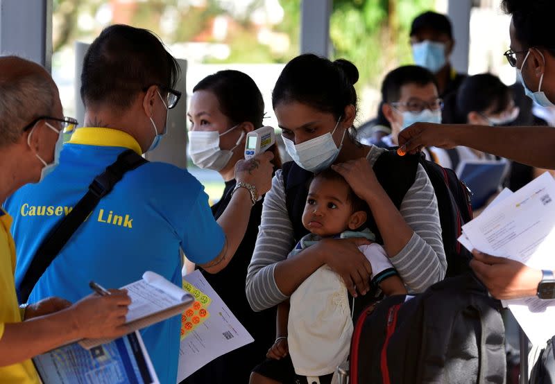 A mother and child get their temperatures checked as they prepare to board a bus back to Malaysia at a station in Singapore