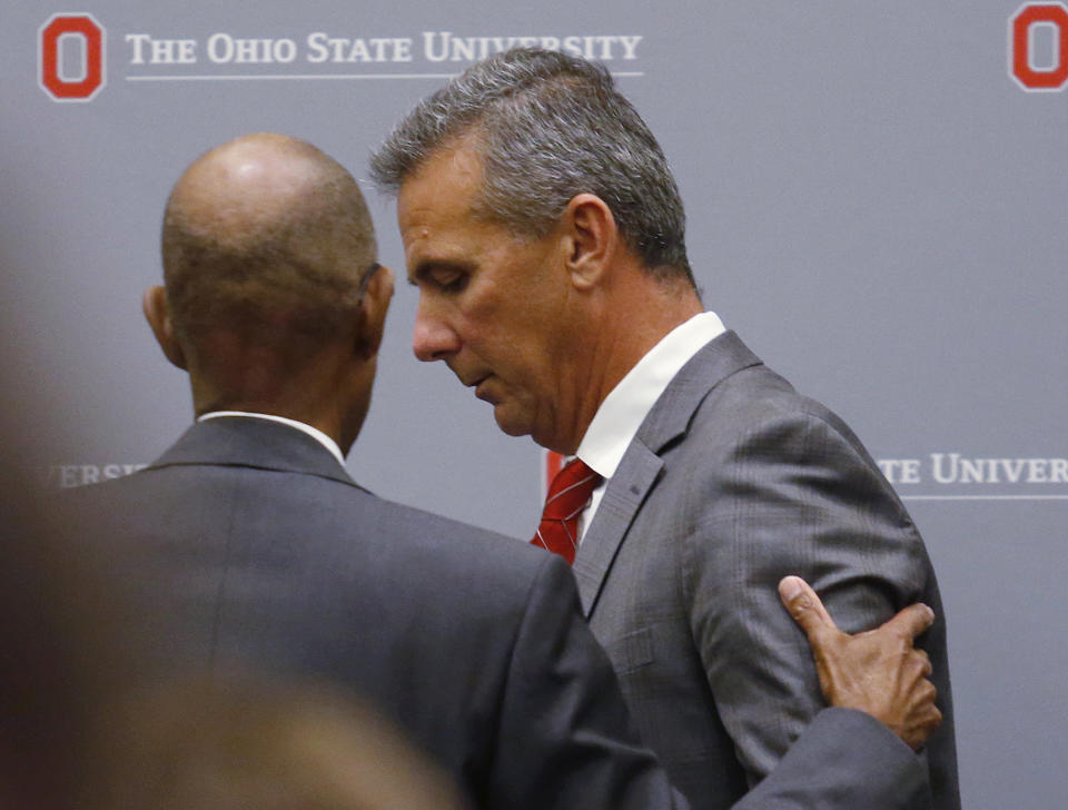 Ohio State University President Michael Drake offers words to football coach Urban Meyer, who leaves the stage following a news conference in Columbus, Ohio, Wednesday, Aug. 22, 2018. Ohio State suspended Meyer on Wednesday for three games for mishandling domestic violence accusations, punishing one of the sport's most prominent leaders for keeping an assistant on staff for several years after the coach's wife accused him of abuse. Athletic director Gene Smith was suspended from Aug. 31 through Sept. 16. (AP Photo/Paul Vernon)