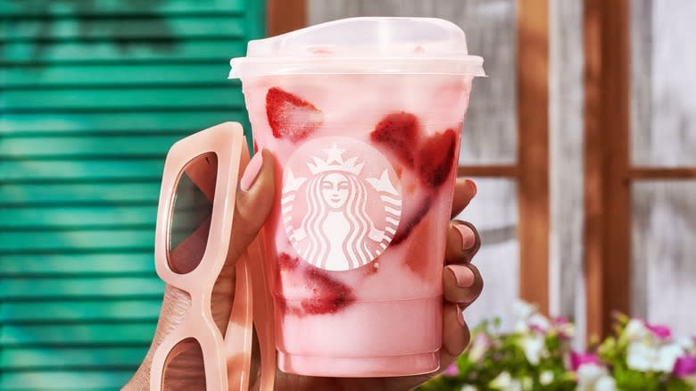 Hand holding a Starbucks strawberry Pink Drink and pink sunglasses