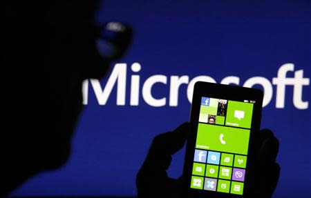 A man is silhouetted against a video screen with Microsoft text as he poses with Nokia Lumia 820 smartphone in this photo illustration taken in the central Bosnian town of Zenica, September 3, 2013. REUTERS/Dado Ruvic