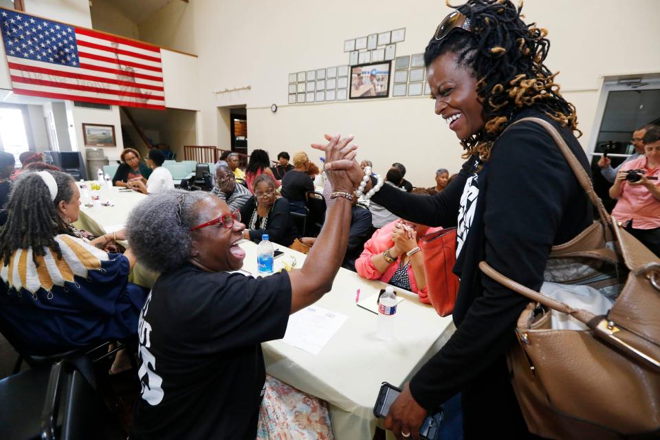 Two women clap hands as others sit around a table.