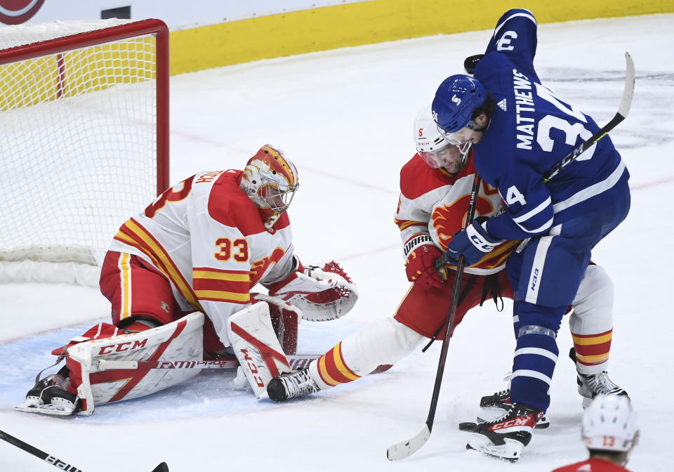 Toronto Maple Leafs centre Auston Matthews (34) gets tied up by Calgary Flames defenseman Mark Giordano (5) as Flames goaltender David Rittich (33) keeps a close eye on the loose puck during third period NHL hockey action in Toronto on Monday, Feb. 22, 2021. (Nathan Denette/The Canadian Press via AP)