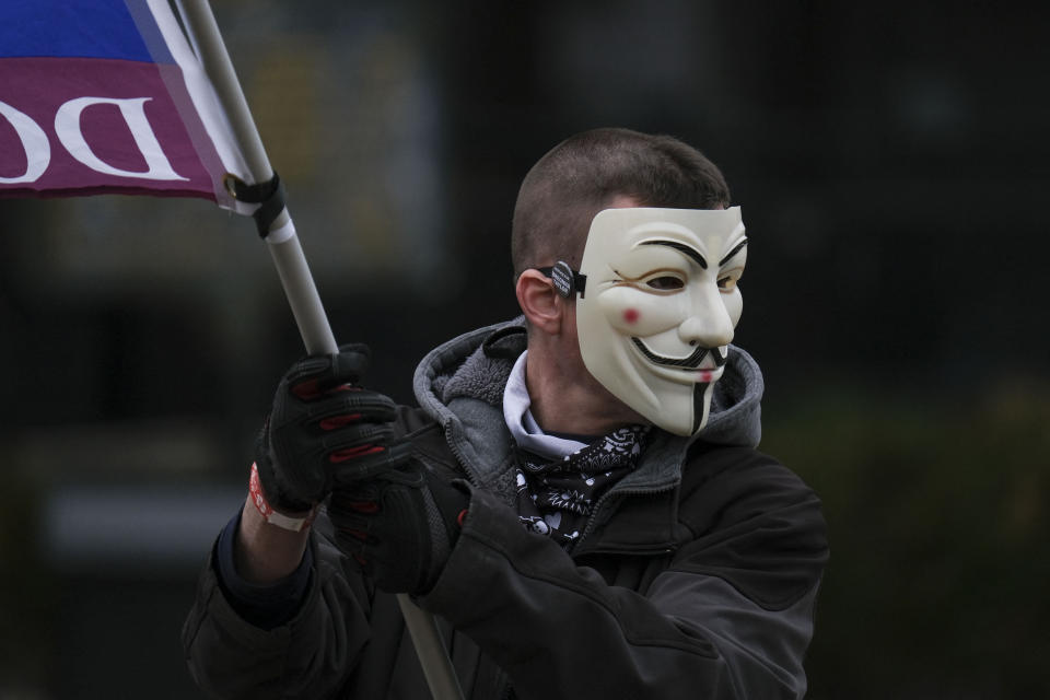 A protestor wearing a Guy Fawkes mask waves a flag during a rally in remembrance on the one year anniversary of Breonna Taylor death in Louisville, Kentucky on March 13, 2021. - Twelve months after the killing -- in which police shot Taylor while looking for a former friend of hers -- only one of three police officers has been charged, and only for endangering Taylor's neighbors by firing wildly. (Photo by Jeff Dean / AFP) (Photo by JEFF DEAN/AFP via Getty Images)