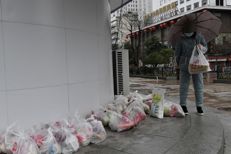 Woman wearing a face mask collects food purchased through group orders at the entrance of a residential compound in Wuhan