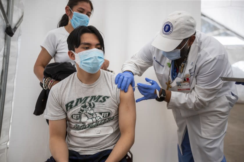 LOS ANGELES, CA - April 15: Dr. Jerry Abraham, director of Kedren Vaccines, right, gives a COVID-19 vaccination to Jose Guzman-Wug, 16, while his mom, Adriana Wug, watches at Kedren Health on Thursday, April 15, 2021 in Los Angeles, CA. Award-winning television producer, Marti Noxon, who's a big fan of Kedren Vaccines, sent an In-N-Out truck to feed 200+ volunteers who help make this vaccine program such a huge success and she did so on the day that vaccines are being made available to all people 16+ in Los Angeles. (Allen J. Schaben / Los Angeles Times)