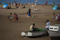 Two migrants sit on a fishing boat as people enjoy the beach in Gran Canaria island, Spain, on Friday, Aug. 21, 2020. Though migrant arrivals to mainland Spain via the Mediterranean Sea have decreased by 50% compared to last year, landings in the Canary Islands have increased by 550% and haven’t been this high in over a decade, raising alarms at the highest levels of the Spanish government. (AP Photo/Emilio Morenatti)