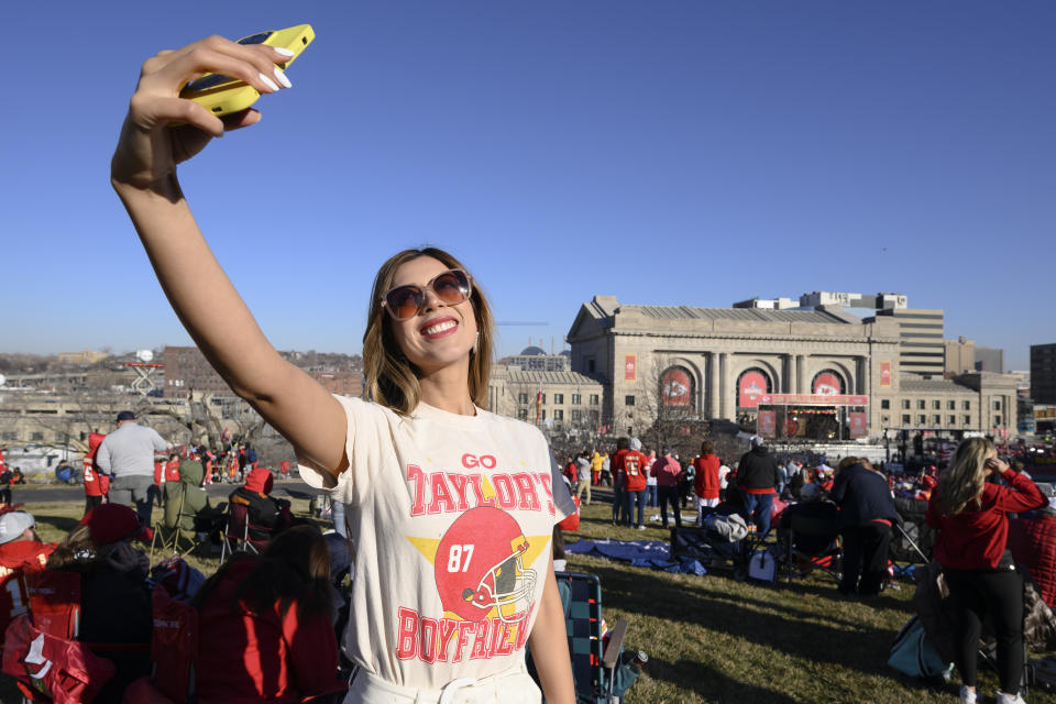 Una fan de los Kansas City Chiefs se toma una selfie frente a Union Station, vistiendo una playera de Taylor Swift, mientras espera que comience el desfile por la victoria del Super Bowl en Kansas City, Missouri, el miércoles 14 de febrero de 2024. (AP Photo/Reed Hoffmann)