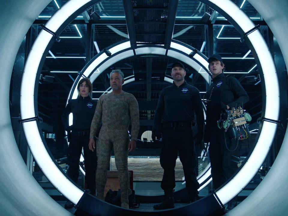 Four people standing in a futuristic looking room lit by circles.