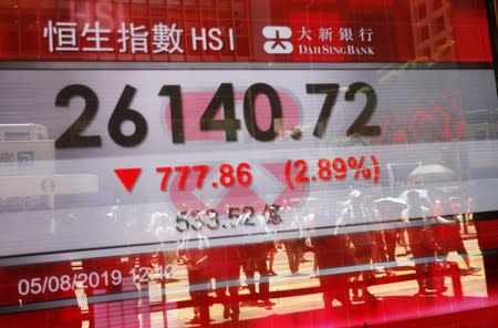 The reflections of pedestrians are seen on a screen displaying the Hang Seng Stock index in Hong Kong