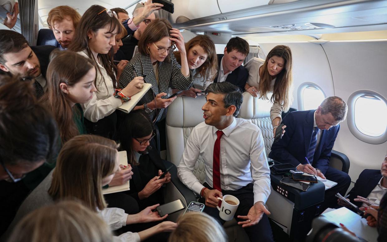 Sunak speaking to journalists on a flight to Warsaw while holding a mug with '10' on it