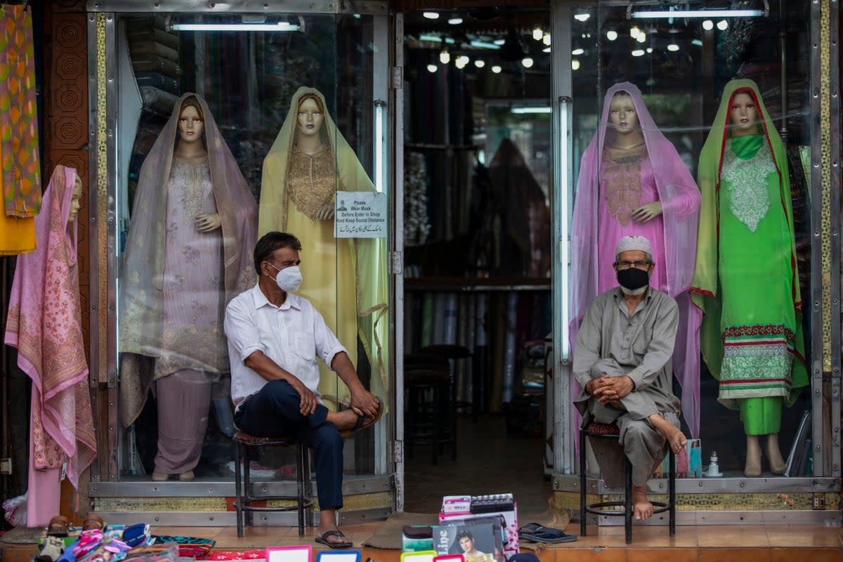 Kashmiri shopkeepers wearing face masks as a precaution against the coronavirus wait for customers outside their shop in Srinagar (Mukhtar Khan / AP)