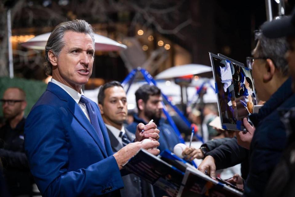 Gov. Gavin Newsom signs a baseball and photos from members of the public attending the red carpet event before the 15th class is inducted into the California Hall of Fame on Tuesday, Dec. 13, 2022, at the California Museum in downtown Sacramento.