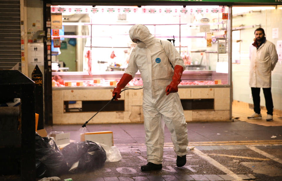 A man wearing a personal protective equipment suit uses a backpack of pressurized spray disinfectant water to remove covid-19 from the street at Queens Market in Upton Park, east London, as the UK continues in lockdown to help curb the spread of the coronavirus. Picture date: Tuesday April 28, 2020.
