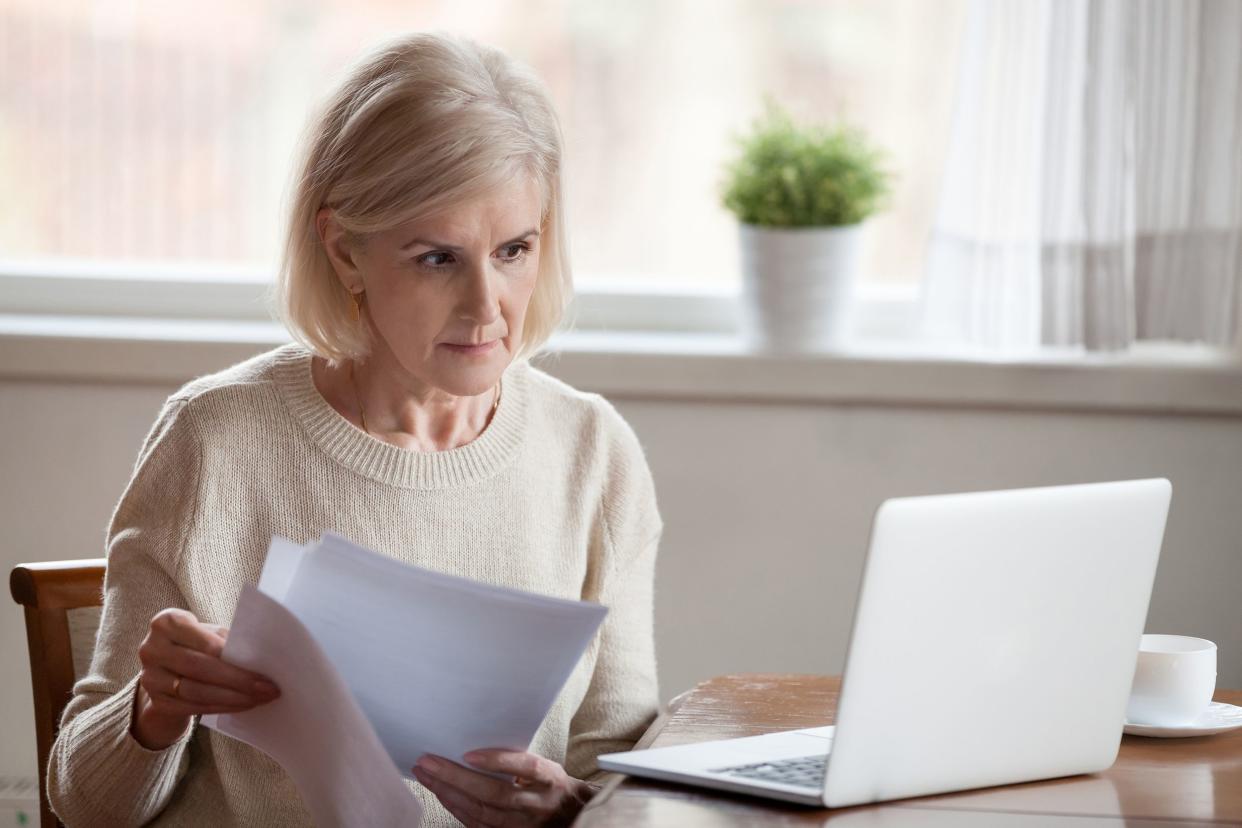 concerned aged female managing bank documents working at laptop