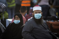 Palestinians wearing face masks sit next to their luggage, as they wait to cross to the Rafah crossing border with Egypt, southern Gaza Strip, Sunday, Sept. 27, 2020. (AP Photo/Khalil Hamra)