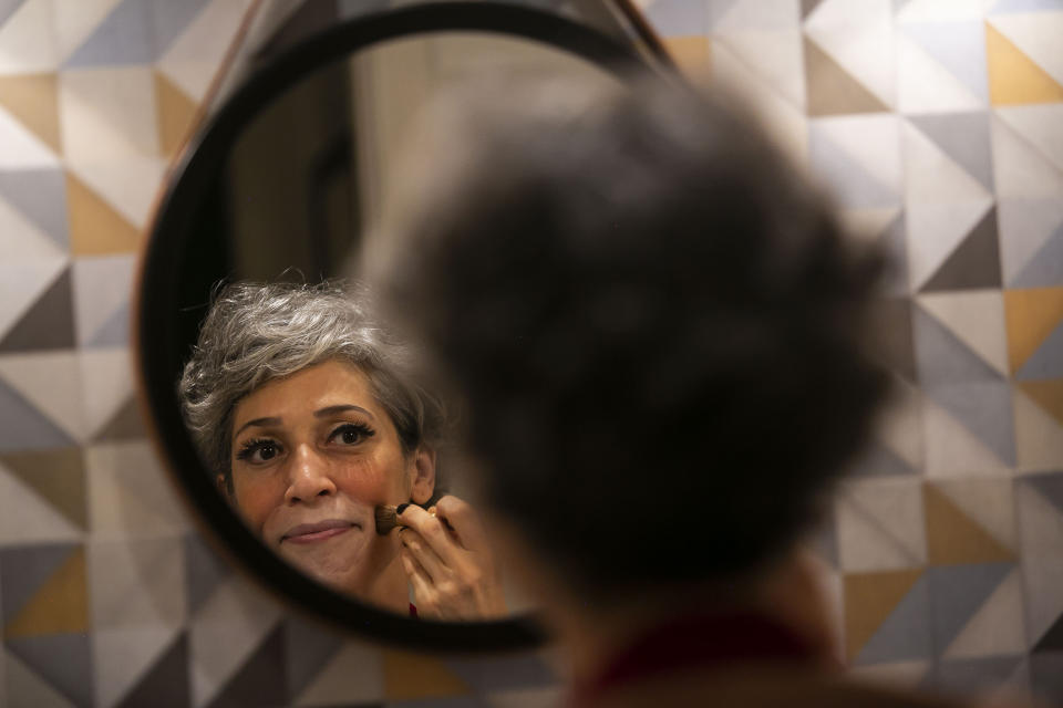 Regina Oliveira puts on show makeup before performing her act for live, online streaming of the "Benditas Genis" women's clown festival at her home during the COVID-19 pandemic in Rio de Janeiro, Brazil, Sunday, March 14, 2021. Oliveira transformed her apartment in the hilltop Santa Teresa neighborhood into a small studio, complete with professional lighting and trapeze, to give classes and presentations. (AP Photo/Bruna Prado)