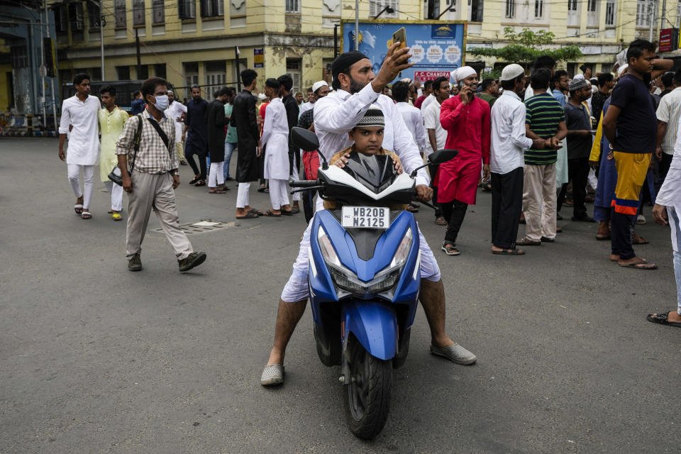 An Indian Muslim with his child on a two wheeler takes photos on his mobile as others block road during protest against the spokesperson of governing Hindu nationalist party as they react to the derogatory references to Islam and the Prophet Muhammad in Kolkata, India, Friday, June 10, 2022. Thousands of Muslims emerging from mosques after Friday prayers held street protests and hurled rocks at the police in some Indian towns and cities over remarks by two officials from India’s ruling party that were derogatory to the Prophet Muhammad. (AP Photo/Bikas Das)
