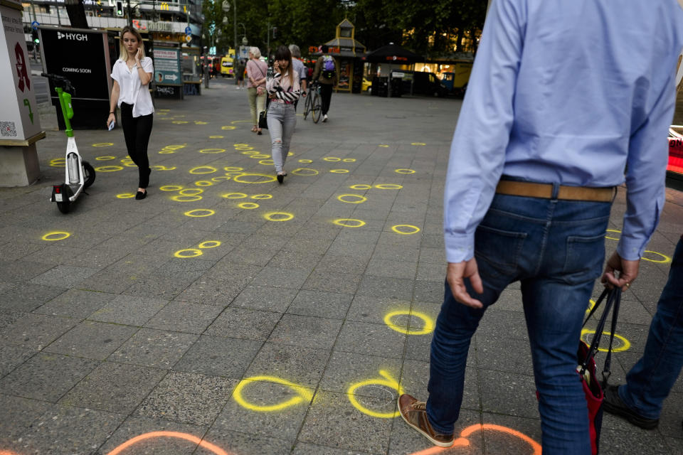 Pedestrians walk over yellow circles painted by investigators to mark evidence and other items on the sidewalk of the street after a car crashed into a crowd of people in central Berlin, Germany, Wednesday, June 8, 2022. Authorities say a teacher was killed and nine people were seriously injured after a man drove a car into a German school group standing in a popular Berlin shopping district. (AP Photo/Markus Schreiber)