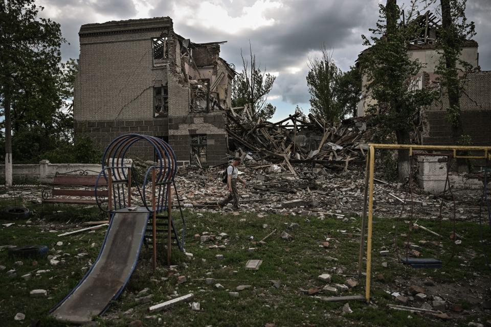 A man walks past a slide and swings in a playground strewn with rubble.